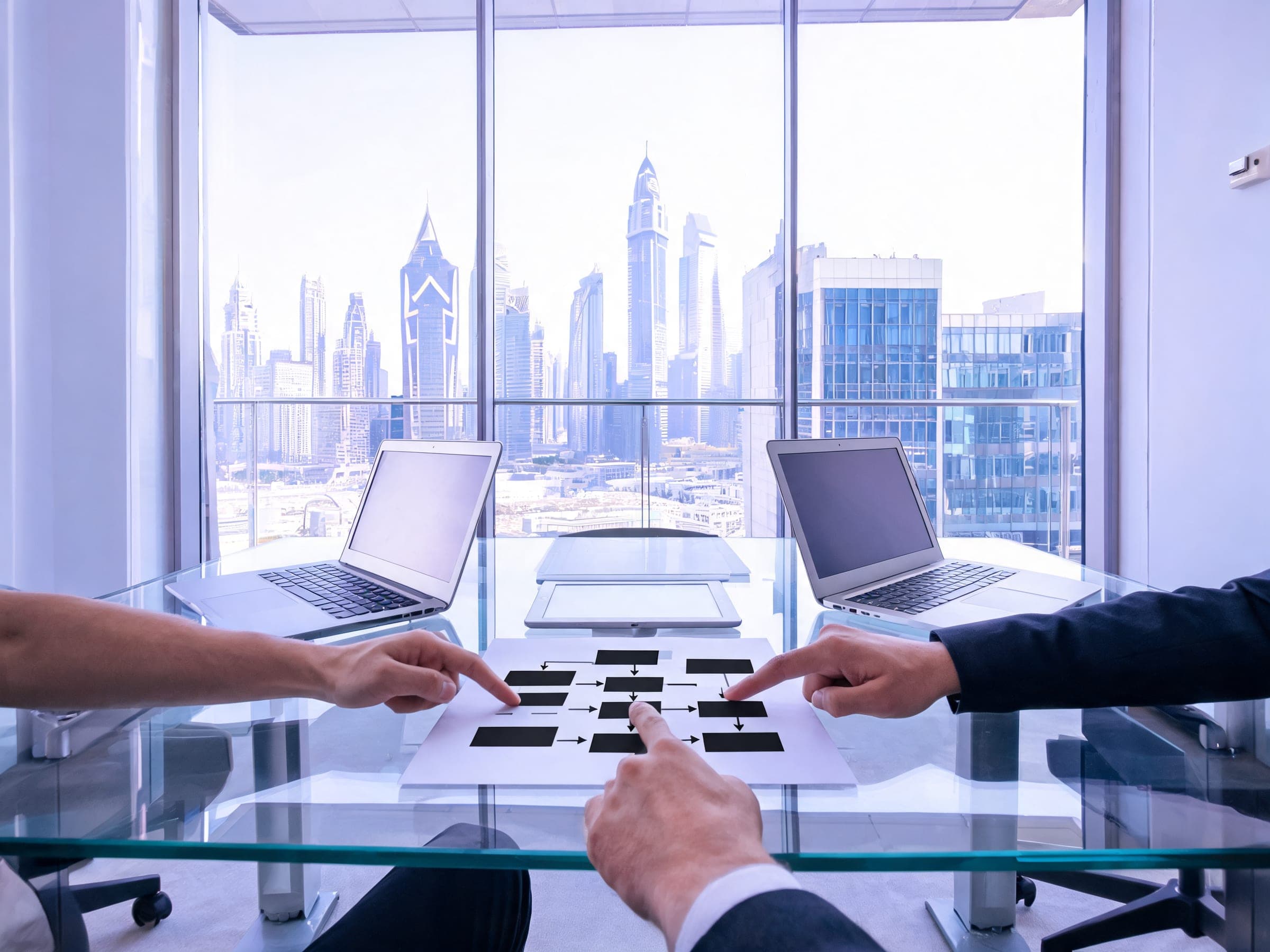 Hands arranging cards on a glass table between two laptops in a DIFC meeting room