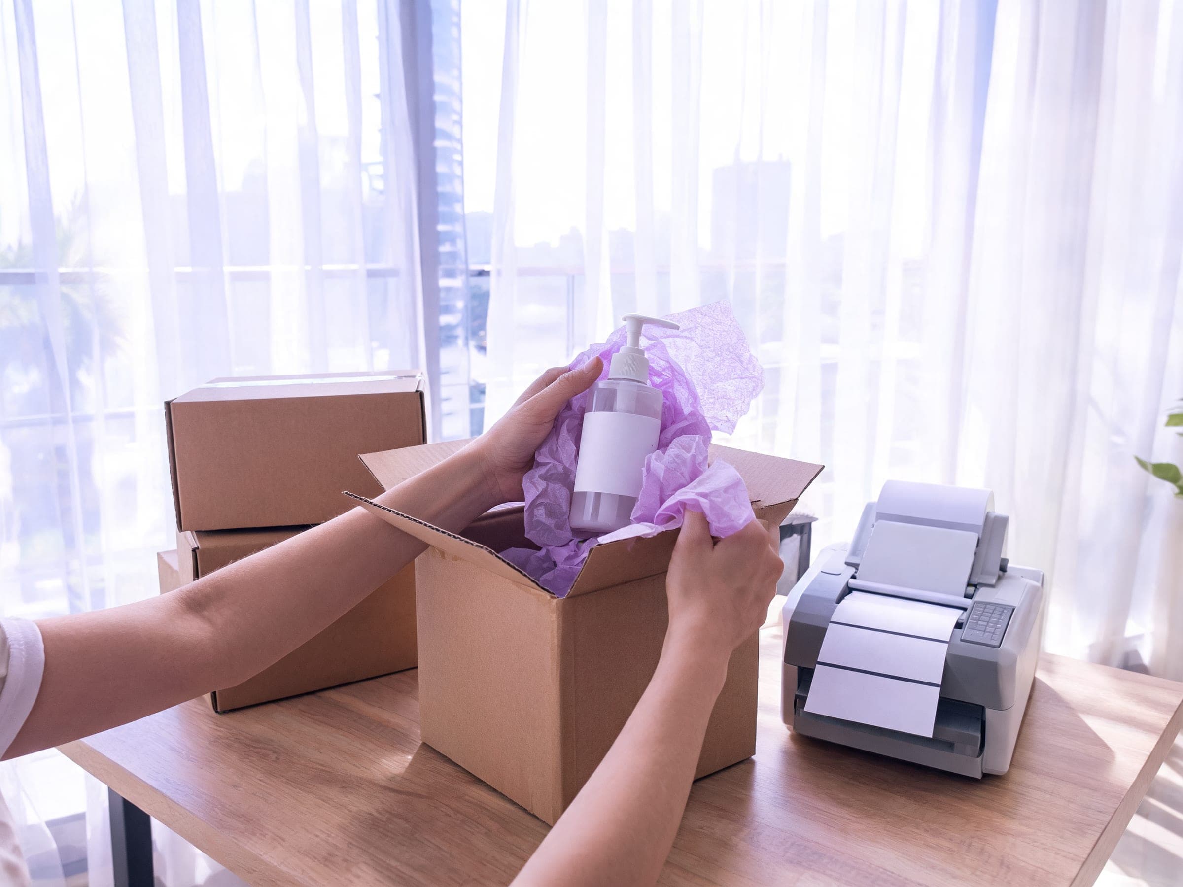 Hands packing an order into a box beside a label printer in a Dubai studio