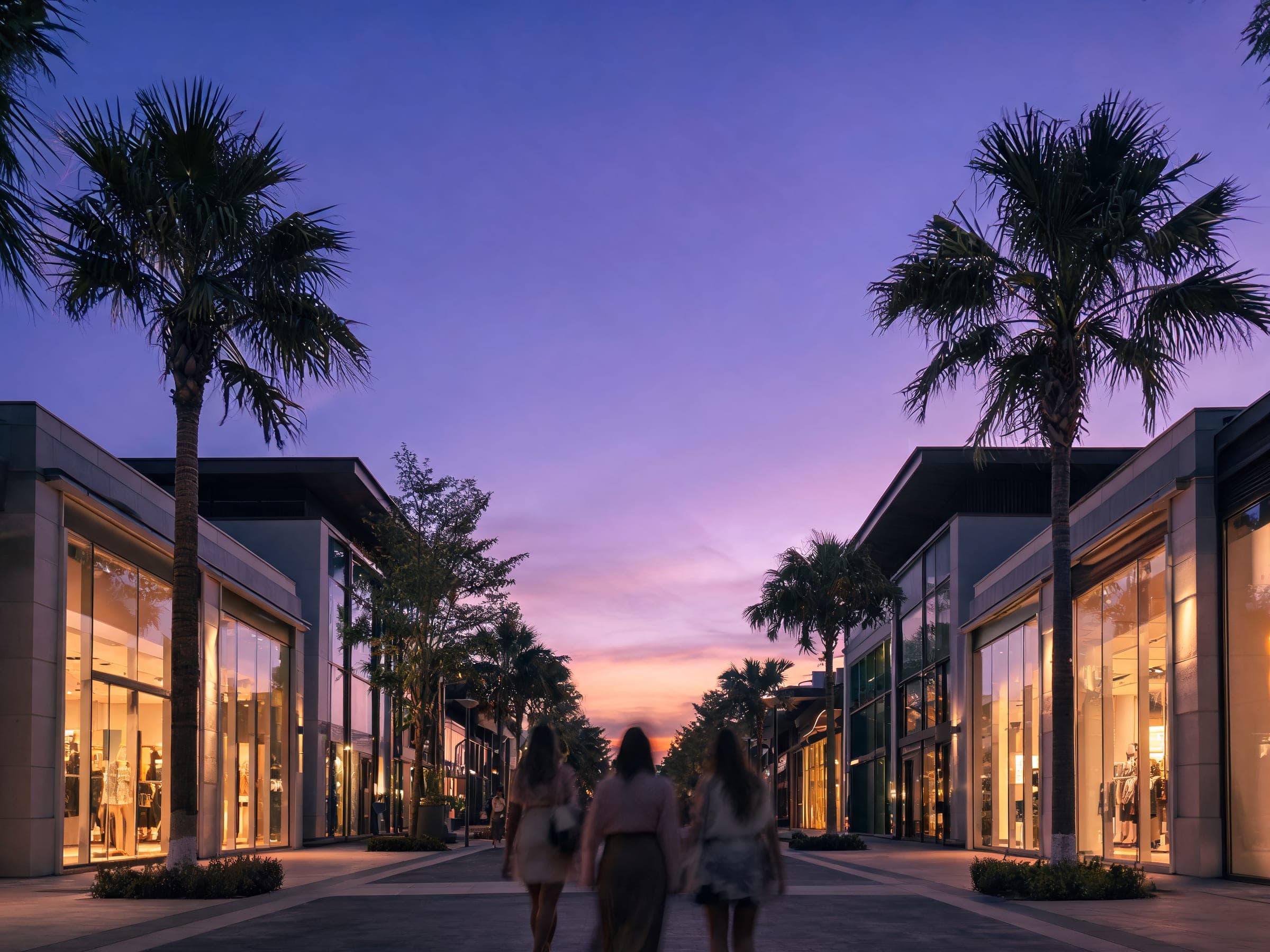 A boutique street lined with palms and lit shopfronts in Dubai at dusk